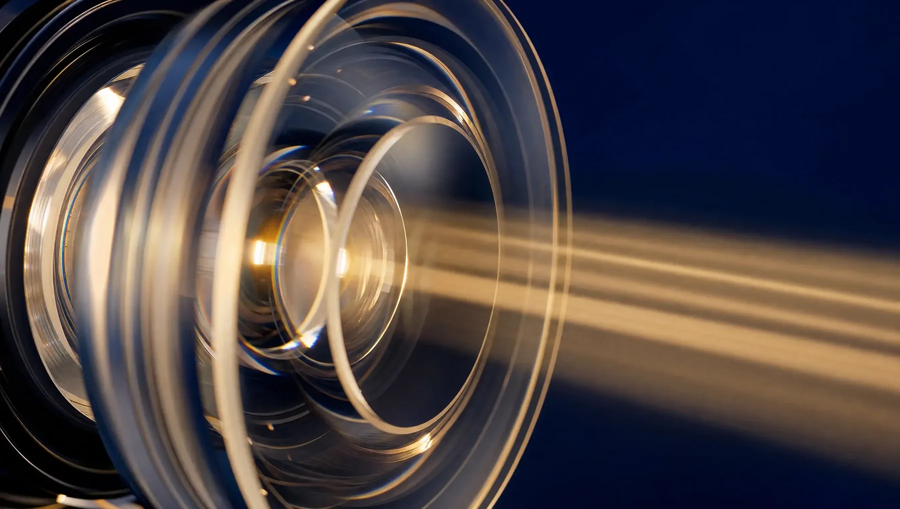 Macro photograph of layered optical glass elements with warm light refracting through them against a deep blue ground